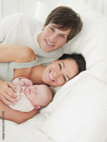 Photo: Smiling parents holding sleeping baby in bed Smiling parents holding sleeping baby in bed