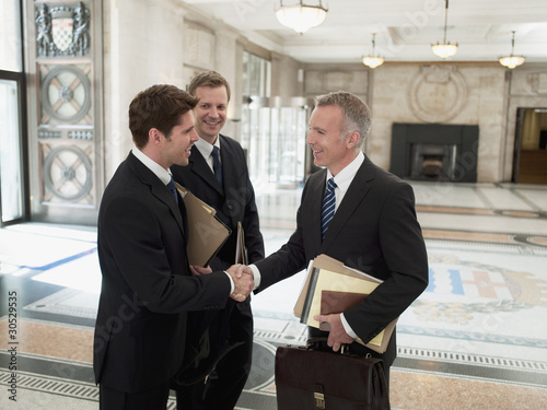 Foto: Smiling lawyers with files shaking hands in lobby Smiling lawyers with files shaking hands in lobby