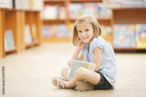 Photo: Girl sitting on floor of library with book Girl sitting on floor of library with book