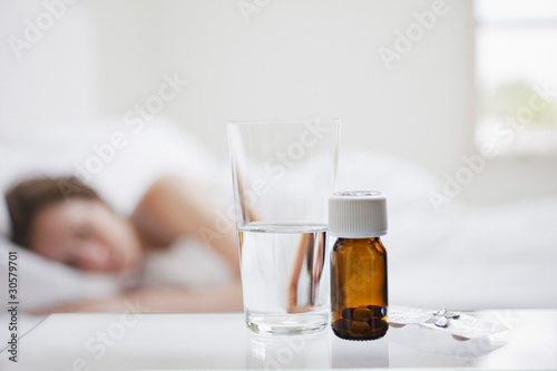 Photo: Close up of pill bottle with sick woman in background Close up of pill bottle with sick woman in background