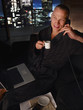 Man in bathrobe with laptop drinking coffee and talking on telephone
