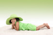 Beautiful Young Girl Laying In the Sand Wearing Big Green Hat