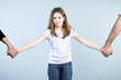 Frowned girl holding her parents hands