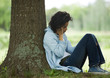 Young woman sitting on ground, leaning against tree