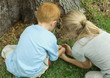 Two children catching small animal at base of tree