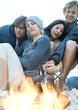 Young adults grilling hotdogs over campfire