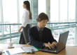 Businessman using laptop, woman walking by in background