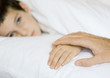 Child lying in bed, father's hand on child's