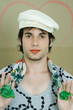Young man wearing lipstick, cap, and scarf, smiling at camera, portrait