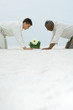 Photo: Two men down on all fours in sand, both looking down at flower growing out of wheat grass Two men down on all fours in sand, both looking down at flower growing out of wheat grass