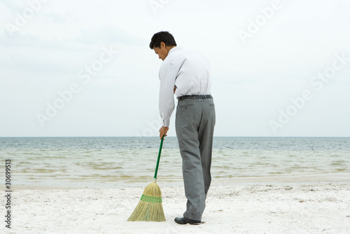 Foto: Man standing on beach sweeping with broom, rear view Man standing on beach sweeping with broom, rear view