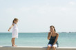 Little girl standing on low wall, watching older sister using cell phone