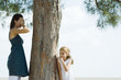 Photo: Two sisters playing hide-and-seek, one covering eyes with hands, the other peeking around tree trunk Two sisters playing hide-and-seek, one covering eyes with hands, the other peeking around tree trunk