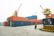 Person riding bicycle past metal storage units, cranes in background