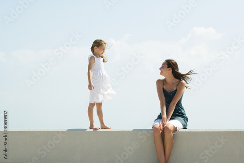 Photo: Little girl walking on ledge toward older sister, seated, both smiling at each other Little girl walking on ledge toward older sister, seated, both smiling at each other