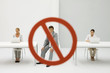 Photo: Two women seated in front of laptop computers, warning sign over man between them, man looking at camera Two women seated in front of laptop computers, warning sign over man between them, man looking at camera