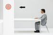 Man sitting at desk, using laptop computer, arrow on wall pointing at bull's-eye