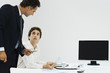 Boss looking over employee's shoulder, employee holding hand over mouthpiece of phone