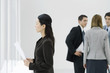 Businesswoman looking out window, holding document, colleagues talking in background