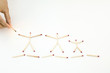 Hand holding lit match up to unlit matches arranged as stick figures