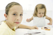 Photo: Girl sitting at table with younger sister, smiling over shoulder at camera Girl sitting at table with younger sister, smiling over shoulder at camera
