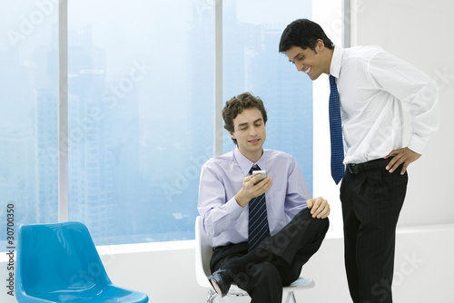 Photo: Young professional showing colleague his cell phone, both smiling Young professional showing colleague his cell phone, both smiling