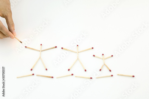 Photo: Hand holding lit match up to unlit matches arranged as stick figures Hand holding lit match up to unlit matches arranged as stick figures