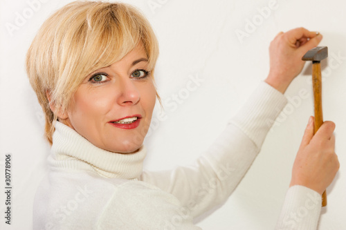 Foto: Frau schlägt einen Nagel in die Wand Frau schlägt einen Nagel in die Wand