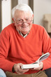 Senior Man Relaxing In Chair At Home Reading Book