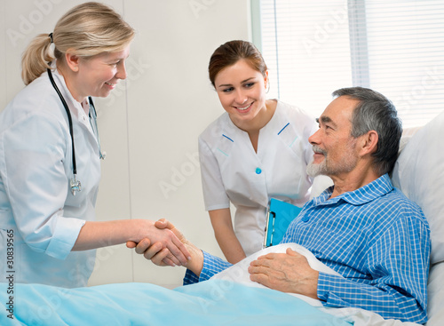 Photo: doctor shakes hands with patient in hospital bed doctor shakes hands with patient in hospital bed