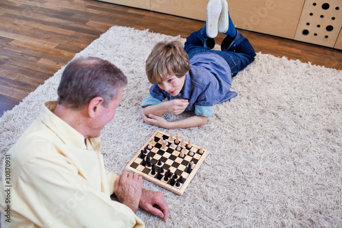 Photo: Grandfather playing chess with grandson on rug Grandfather playing chess with grandson on rug