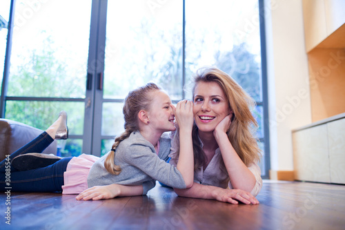 Photo: Mother and daughter laying on wooden floor whispering Mother and daughter laying on wooden floor whispering