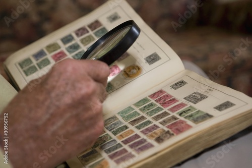 Foto: Senior man looks at stamp collection with magnifying glass Senior man looks at stamp collection with magnifying glass