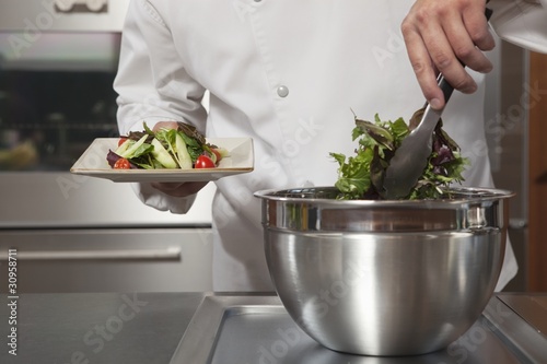 Foto: Mid- adult chef lifts leaf vegetables onto side plate Mid- adult chef lifts leaf vegetables onto side plate