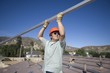 A man lifting a large metal pole on a roof top