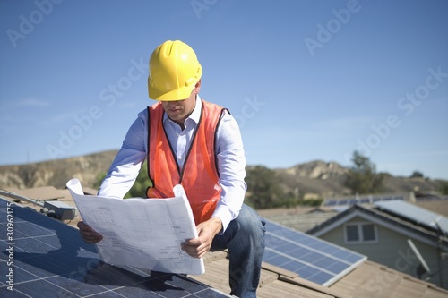 Photo: A business man on a solar panalled rooftop looking at plans A business man on a solar panalled rooftop looking at plans