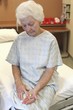 Photo: An old lady in a hospital gown, sitting on a bed, looking down at several pills in her hand An old lady in a hospital gown, sitting on a bed, looking down at several pills in her hand