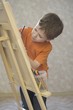 A young boy drawing onto a canvas, with a pot of coloured pencils stood on the ledge of the canvas