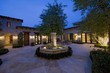 Photo: House exterior at night with a fountain, patio furniture and trees, one in which is lit with fairy lights House exterior at night with a fountain, patio furniture and trees, one in which is lit with fairy lights