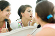 Young female friends looking at mirror, putting on make-up
