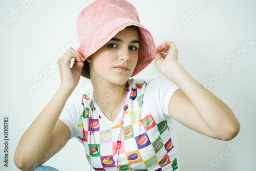 Photo: Teen girl putting on hat, portrait Teen girl putting on hat, portrait