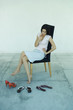 Photo: Young woman sitting in chair, looking down at three pairs of shoes, full length portrait Young woman sitting in chair, looking down at three pairs of shoes, full length portrait