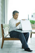 Mature man sitting on bench, opening briefcase, full length
