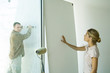 Man holding level against wall and woman putting hand against wall board
