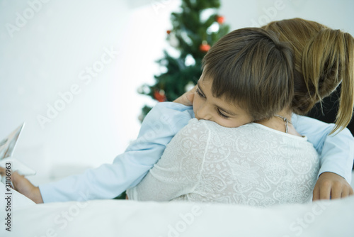 Photo: Mother sitting on sofa, holding boy in arms, Christmas tree in background, boy holding star Mother sitting on sofa, holding boy in arms, Christmas tree in background, boy holding star