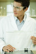 Researcher wearing protective goggles picking up Petri dish, looking away