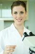 Female lab worker with microscope, holding up slide, smiling at camera, portrait