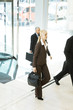 Young businesswoman entering lobby, carrying briefcase, man in background
