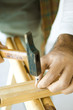 Man hammering nail into piece of wood, close-up of hands