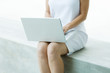 Woman sitting on low wall, using laptop computer, cropped view